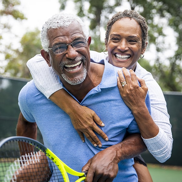 A mature couple playfully embrace on a tennis court and smile