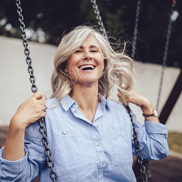 A mature woman ridding a swing in the park smiling