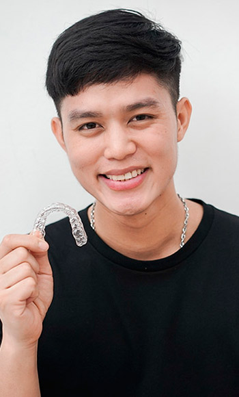 A young man holding some Invisalign aligners while smiling