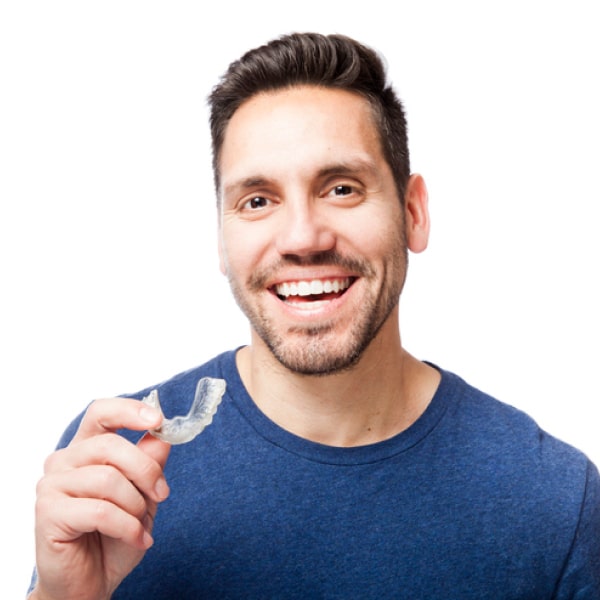 A man smiles and holds a clear aligner tray